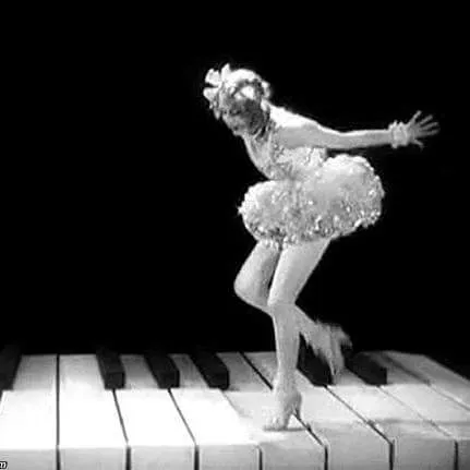 Photographie en noir et blanc d'une danseuse miniature en tutu, dansant avec dynamisme sur les touches géantes d'un piano.
