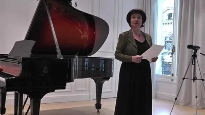 Sabine Miniconi sur scène, debout devant un piano à queue, tenant ses notes lors d'une audition